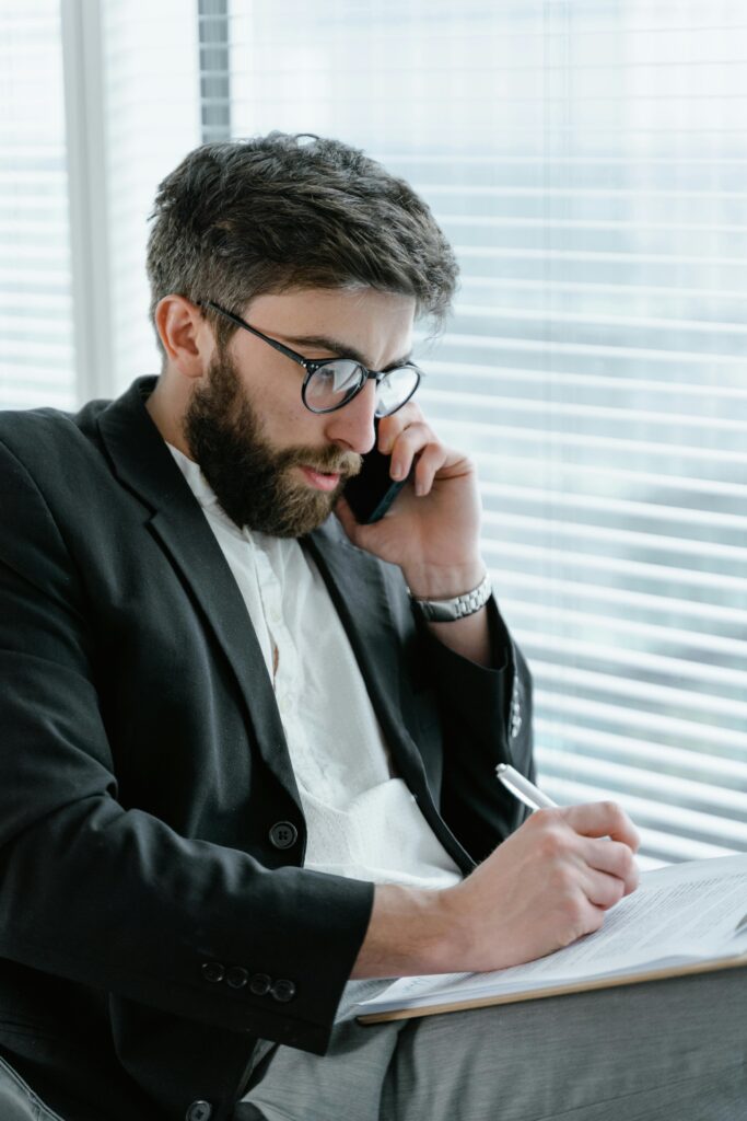 pexels-photo-7567553-7567553 Focused businessman in office, analyzing documents while on a phone call.
